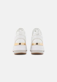 Hvite sneakers med en glatt skinnoverdel og en gullmetallaccent på hælen. Har en polstret såle og en teksturert gummiyttersåle.