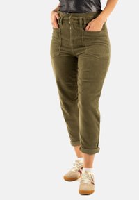 Pantalones de pana verde oliva de cintura alta, con cinco bolsillos y puños enrollados, combinados con zapatillas ligeras que tienen acentos en beige y burdeos.