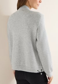 Šedá mikina s kulatým výstřihem, žebrovanými manžetami a ozdobným stahovacím lemem. Měkká textura a volný střih.