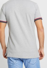 Camiseta de manga corta gris con acentos de rayas rojas y marino en las mangas. Hecha de una tela suave, con un dobladillo recto y una abertura en los laterales.