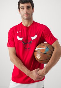Rød Nike T-shirt med en sort og hvid tyr grafik, korte ærmer, parret med en basketball med et multifarvet design og logo.