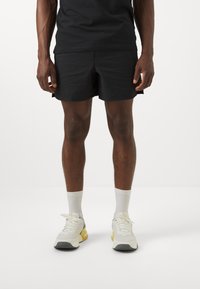 Shorts neri con texture a griglia, abbinati a calzettoni bianchi e sneakers chiare con dettagli gialli e grigi.