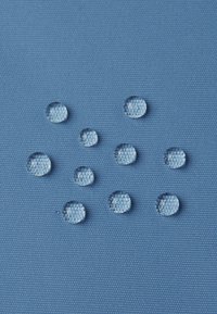 Klare Wassertropfen auf einer strukturierten blauen Oberfläche, die kreisförmige Formen und unterschiedliche Größen zeigen, mit einem glatten Glanz.