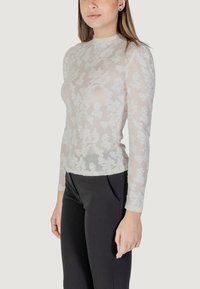 Top bianco a maniche lunghe trasparente con design in pizzo floreale, collo alto, silhouette aderente, abbinato a pantaloni neri su misura.