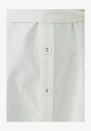 Valge riietus, millel on nööpidega disain, kus on kaks nööpi ja volditud tekstuur alt. Materjal näeb sile välja, kerge läikega.