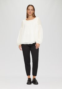 Witte, vloeiende blouse met oversized, geplooide mouwen en een vierkante halslijn, gecombineerd met zwarte, strakke pantalons en glanzende zwarte instappers.