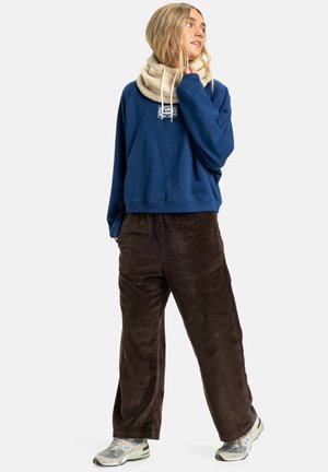 Navy blue sweatshirt with a logo, paired with brown corduroy pants and a beige textured scarf. Footwear: light grey sneakers.