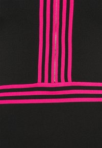Tissu noir avec des rayures roses vives verticales et horizontales se croisant au niveau d'une fermeture éclair, créant un motif géométrique sur le textile.