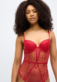 Κόκκινη διαφανής γυναικεία εσώρουχα με μοτίβα καρδιών, ενισχυμένα μπούστα, ρυθμιζόμενες τιράντες και διακοσμητικό περίγραμμα. Ο σχεδιασμός διαθέτει εφαρμοστή σιλουέτα.
