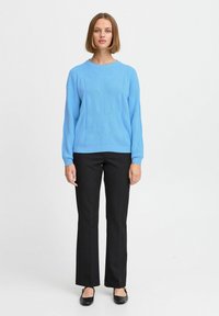 Maglione blu lavorato a maglia con un motivo testurizzato, abbinato a pantaloni neri e scarpe flat. Il maglione ha un collo rotondo e maniche lunghe.