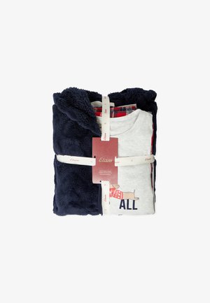 Set piegato composto da giacca in fleece navy, pantaloni a quadri rossi e maglietta grigia chiara con una grafica di un cane, tenuto da nastri bianchi con logo e un'etichetta rossa.