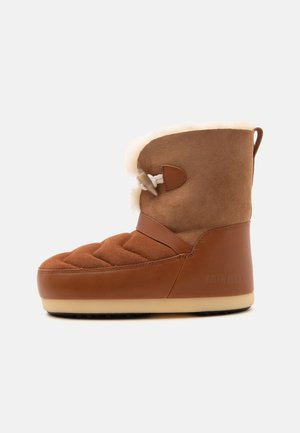 Botte d’hiver marron avec devant matelassé, partie inférieure en cuir, doublure en laine et lacet à bouton-pression sur le côté, vue de profil sur fond blanc.