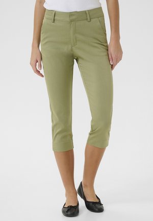 Pantaloni cropped verde chiaro realizzati in un tessuto liscio, con vita aderente, tasche laterali e risvolti. Abbinati a scarpe nere senza tacco.