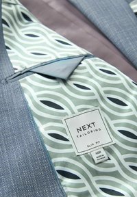 Futter eines Sakko mit geometrischem Muster und angenähtem Etikett mit der Aufschrift "NEXT Tailoring Slim Fit 40R Made in Vietnam."