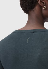Top ribbed verde scuro con scollo ampio e un sottile ricamo di teschio di capra sul retro. Tessuto morbido e design aderente.