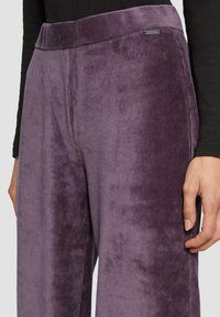 Corduroy broek in dieppaars met een zachte textuur. Heeft een brede tailleband en een subtiele ribbelstructuur. Hand gepositioneerd op het rechterbeen.