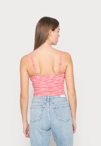 Top cropped justo rosa com alças finas, tecido texturizado com um padrão mesclado. Usado com jeans de cintura alta em azul claro.