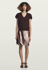 Maglione a V in maglia marrone, mini gonna in paillettes color oro rosa metallico, pochette nera e sandali neri con cinturino. Tessuto liscio e design aderente.