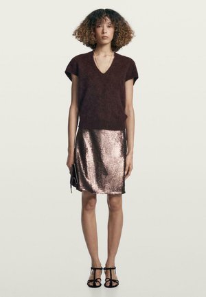 Maglione a V in maglia marrone, mini gonna in paillettes color oro rosa metallico, pochette nera e sandali neri con cinturino. Tessuto liscio e design aderente.