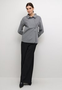 Gray striped shirt with a large collar, buttons down the front, and long sleeves, paired with black wide-leg pants and pointed black shoes.
