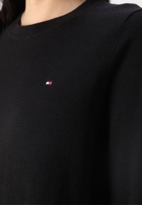 Maglione nero a maglia con scollo rotondo, caratterizzato da un piccolo logo ricamato in rosso, bianco e blu nella zona sinistra del petto.