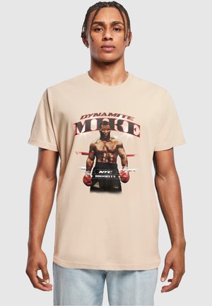 Beige pamut póló, grafikával, amelyen egy ökölvívó látható piros kesztyűkkel, a "DYNAMITE MIKE" szöveggel és a "NYC BROOKLYN" felirattal kiemelt betűkkel.
