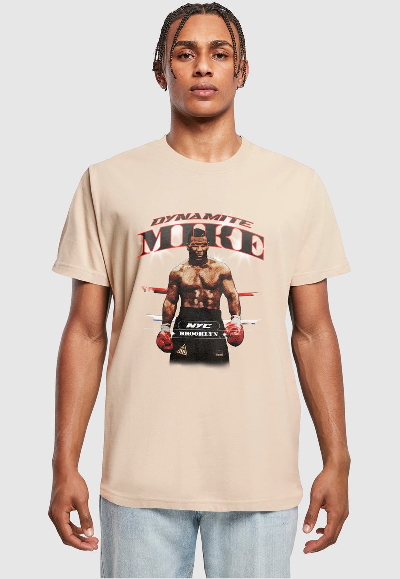 Tricou din bumbac bej, prezentând o imprimare grafică cu un boxer purtând mănuși roșii, textul „DYNAMITE MIKE” și „NYC BROOKLYN” în litere îngroșate.