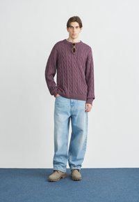 Μωβ πουλόβερ με πλέξη καλτσοδέτα και στρογγυλή λαιμόκοψη, συνδυασμένο με ανοιχτόχρωμα φαρδιά τζιν και μπεζ μποτάκια μέχρι τον αστράγαλο. Λείο ύφασμα και άνετη εφαρμογή.