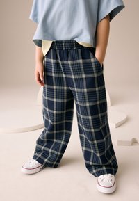 Pantaloni a gamba larga a quadri blu navy con motivo a scacchi e tasche, abbinati a una maglia oversize azzurro chiaro e sneaker bianche.