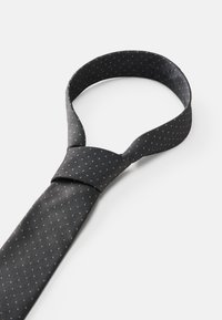 Mustat solmiot, joissa on teksturoitu kuvio pienistä valkoisista pisteistä. Niissä on klassinen muoto ja sileä, kiiltävä kangaspinta.