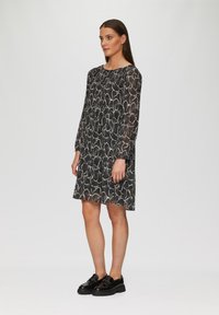 Robe à motif noir et blanc avec des manches longues, un col rond et une coupe ample, assortie à des chaussures noires brillantes. Texture lisse.