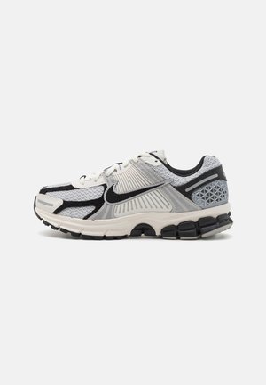 Nike-Laufschuh in Schwarz, Grau und Weiß. Merkmale sind ein Obermaterial aus Mesh, ein strukturiertes Design, eine dicke gepolsterte Sohle und reflektierende Akzente.