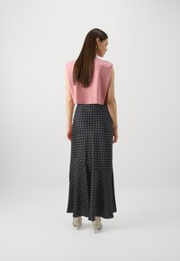 Rosa avkortet topp med korte ermer, kombinert med et langt, svart skjørt med prikker. Skjørtet har en flagrende kant og er laget av et lett stoff.