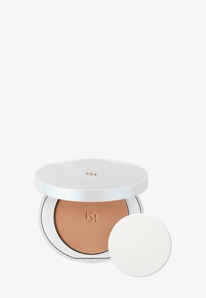 Maquillage en poudre compacte avec un boîtier rond blanc, une poudre pressée beige, et une éponge applicatrice ronde blanche séparée.