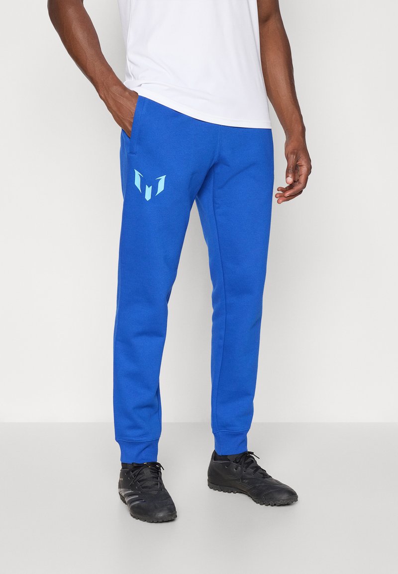 Mėlyni sportiniai džinsai, pagaminti iš minkštos medžiagos, su šoninėmis kišenėmis ir šviesiai mėlynu grafiniu logotipu kairėje šlaunyje. Elastingi rankogaliai ant kulkšnių.