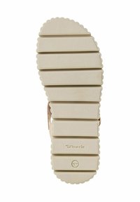 Beżowa podeszwa sandała z gumy z teksturowanym, żeberkowym wzorem i falistymi krawędziami, z wytłoczonym logo marki blisko pięty.