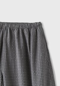 Pantalon en tissu gris à carreaux avec taille élastique et détails de coutures froncées visibles sur fond blanc.
