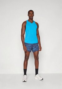Camiseta deportiva sin mangas azul combinada con pantalones cortos azules con estampado. Zapatillas blancas y calcetines negros completan el conjunto. Diseño sencillo y funcional.