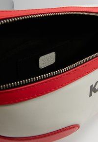 Bolso de cuero blanco y rojo con cierre de cremallera, que presenta un interior negro y una etiqueta de logo plateada etiquetada como "KARL LAGERFELD."