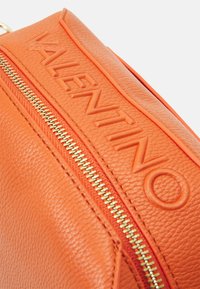 Borsa in pelle arancione con logo "VALENTINO" in rilievo, superficie testurizzata e dettaglio zip dorato. Design compatto con forma strutturata.