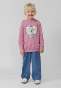Roze hoodie met een grafisch ontwerp van twee kittens in een hart met de tekst "VRIENDEN" eronder. Gecombineerd met blauwe wijde jeans.