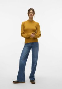Senapsgul tröja med texturerade puffärmar, matchad med utsvängda blå jeans och bruna ankelboots. Enkla, rena linjer.