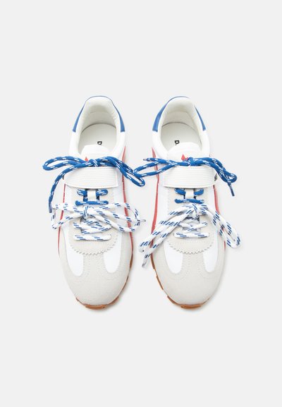Paire de baskets blanches avec des lacets à motif bleu et blanc, des bandes latérales rouges, des accents bleus au talon et des brides velcro blanches réglables.