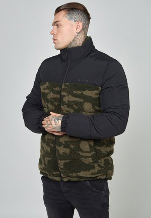Pufferjakke med en sort nylon overdel og en grøn camouflage fleece nederdel. Har en høj krave og lynlås lukning. Teksturerede materialer.