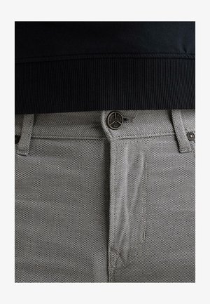 Približni prikaz sivih teksturiranih traperica s metalnim gumbom na kojem piše "Legend Jeans PME" i crnim rebrastim pojasevima iznad.