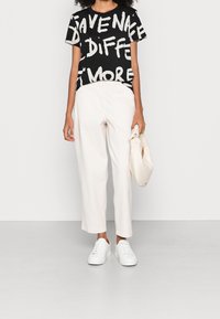 Czarny t-shirt z białym, pogrubionym napisem, zestawiony z kremowymi spodniami o szerokich nogawkach. Akcesoria to teksturowana torba i białe trampki.