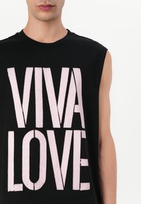 Svart ermeløs t-skjorte med store rosa blokkbokstaver "VIVA LOVE." Laget av mykt bomullsmateriale med en behagelig passform.