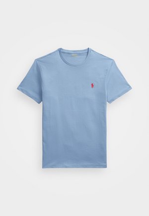 T-shirt en coton bleu clair à manches courtes, col rond, avec un petit logo rouge sur la poitrine gauche. Texture lisse, coupe décontractée.
