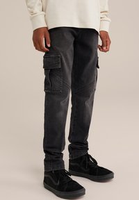 Cargo hlače v temno sivi denimu z več žepi, ožji kroj in teksturirano tkanino. Nosite z črnimi supergami.