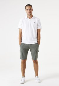Witte polo shirt, groene cargoshorts met zijzakken en witte sneakers. Korte mouwen, casual pasvorm en een gladde textuur.